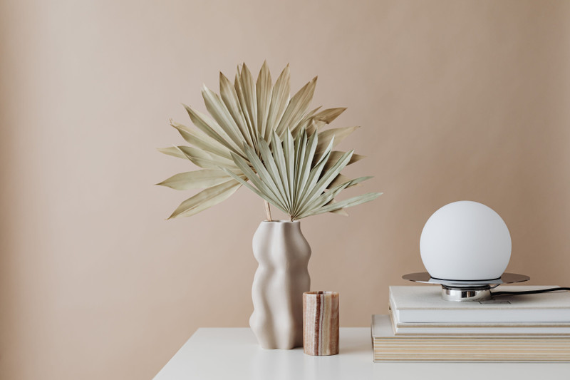 Dried palm leaves in a round vase on a beige shelf.