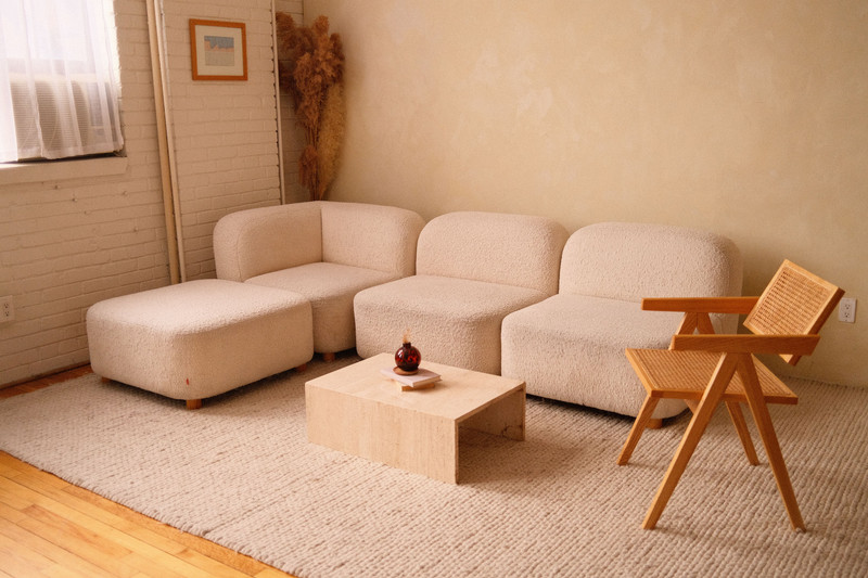 A warm cream living room with a low boucle sofa and a cane chair.