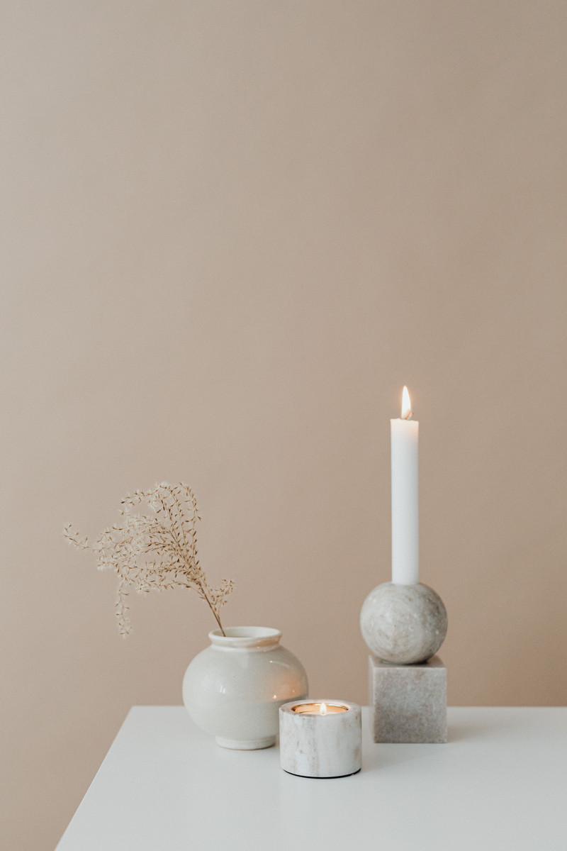 A lit taper on a blush table with a small vase.