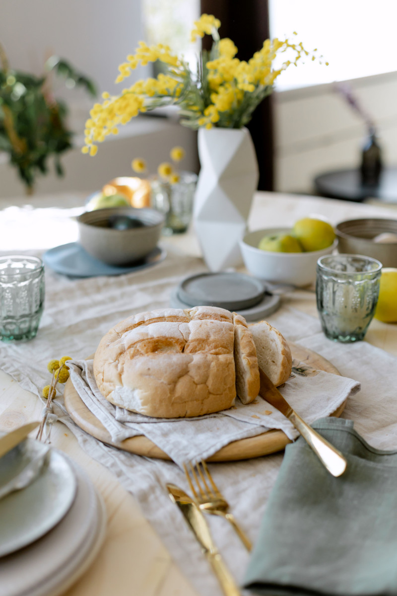 A laid table with bread, linen napkins and yellow flowers.